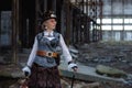 Elderly lady in a steampunk costume at an abandoned factory with arms in hand