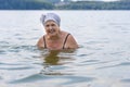 An elderly lady swims in a calm lake. Aged woman enjoying swimming in warm lake water at the resort