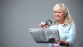 Elderly lady trying to read newspaper with magnifying glass, poor vision problem