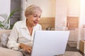 An elderly lady using a laptop. Portrait of beautiful older woman working laptop computer indoors. Senior woman sitting at sofa Royalty Free Stock Photo