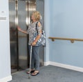 Elderly lady using her walking stick to balance waiting for the elevator