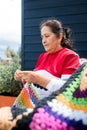 Elderly latin woman with crafts skills knitting a colorful blanket outside her country house. Low angle view