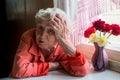 Elderly lone woman looks sadly sitting near the window. Royalty Free Stock Photo