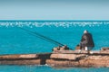 An elderly lonely man is fishing on a sea pier.