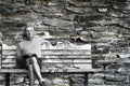 Elderly lonely man sits on bench with old grungy stone brick wall in the background