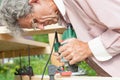 Elderly male carpenter with glasses holds a milling machine in his hands, bending over it and leads through a wooden beam of a