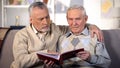 Elderly male friends watching album photos together, family memories, past