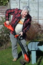 Elderly male gardener trimming grass edges.