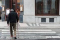 An elderly male with a walking stick slowly walks across a crosswalk in the middle of a city alone Royalty Free Stock Photo