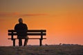 elderly man on bench, profile facing orangehued horizon Royalty Free Stock Photo