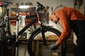 Elderly man bike mechanic repairs bicycle in workshop or garage. Portrait of man wearing apron fixes cycle wheel. Bike Royalty Free Stock Photo