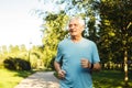 An elderly man in a blue T-shirt is jogging through a summer park. Royalty Free Stock Photo