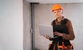 Elderly man in builder safety helmet looking at the camera and typing at laptop in home interior Royalty Free Stock Photo