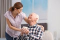 Elderly man with cup of tea near female caregiver at home.