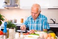 Elderly man cuts vegetables for salad at the table in the kitchen Royalty Free Stock Photo