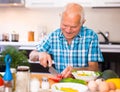 elderly man cuts vegetables for salad at the table in the kitchen Royalty Free Stock Photo