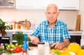 elderly man cuts vegetables for salad at the table in the kitchen Royalty Free Stock Photo