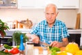 Elderly man cuts vegetables for salad at the table in the kitchen Royalty Free Stock Photo