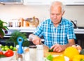 elderly man cuts vegetables for salad at the table in the kitchen Royalty Free Stock Photo