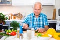 elderly man cuts vegetables for salad at the table in the kitchen Royalty Free Stock Photo