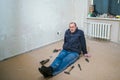 An elderly man in dirty clothes sits on the floor next to hand tools. Tired worker performs repairs in the apartment. The old Royalty Free Stock Photo