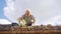 an elderly man dismantles the old brickwork and lays new bricks on the roof.