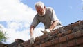 An elderly man dismantles the old brickwork and lays new bricks on the roof.