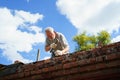 an elderly man dismantles the old brickwork and lays new bricks on the roof. Royalty Free Stock Photo