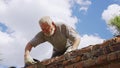 An elderly man dismantles the old brickwork and lays new bricks on the roof.