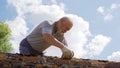 an elderly man dismantles the old brickwork and lays new bricks on the roof.