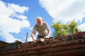 an elderly man dismantles the old brickwork and lays new bricks on the roof.