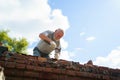 an elderly man dismantles the old brickwork and lays new bricks on the roof.