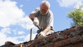 an elderly man dismantles the old brickwork and lays new bricks on the roof.