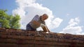 an elderly man dismantles the old brickwork and lays new bricks on the roof.