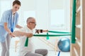 Elderly man doing gymnastic exercises with female physiotherapist