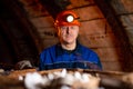 An elderly man dressed in work overalls and a helmet stands near the old inverted vogonetki. Miner Royalty Free Stock Photo