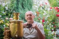 An elderly man drinks tea next to a rare samovar. A man with a cup of tea in his hands sits in a flowering garden near a