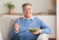Elderly man eating vegetable salad smiling sitting on sofa Royalty Free Stock Photo