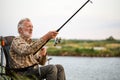 Elderly man fishing outside in evening on lake in summer sitting on chair Royalty Free Stock Photo