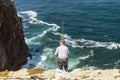 Elderly man fishing with a rod on high cliffs of Sao Vicente Cape, Portugal