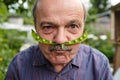 An elderly man is fooling around. He holds a pea pod near his face like a mustache Royalty Free Stock Photo