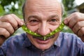 An elderly man is fooling around. He holds a pea pod near his face like a mustache Royalty Free Stock Photo