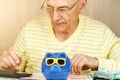 Elderly man in glasses counts on calculator at piggy bank Royalty Free Stock Photo