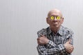 An elderly man with glasses on a gray background crossed his arms over his chest, and sits in his glasses bitcoin sign. Royalty Free Stock Photo