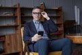 Elderly man in glasses working on mobile phone, sitting on chair in office Royalty Free Stock Photo