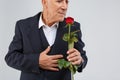 An elderly man on a white background, wearing a black elegant suit, smells a fragrant rose in his hand. Royalty Free Stock Photo