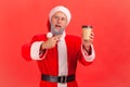 Elderly man with gray beard wearing santa claus costume pointing at coffee, drink with caffeine