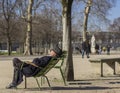 An elderly man in a hat is sleeping in the sun in the park