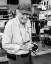 Elderly man holding a digital camera in his hand while smiling for the camera.