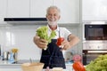 Elderly man holding fresh sweet red bell pepper and green leaf vegetable for making salad, senior man cooking healthy food with Royalty Free Stock Photo